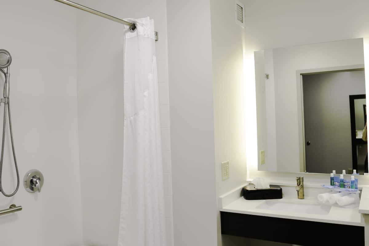 Un baño con ducha, lavamanos y artículos de aseo, y un espejo.
