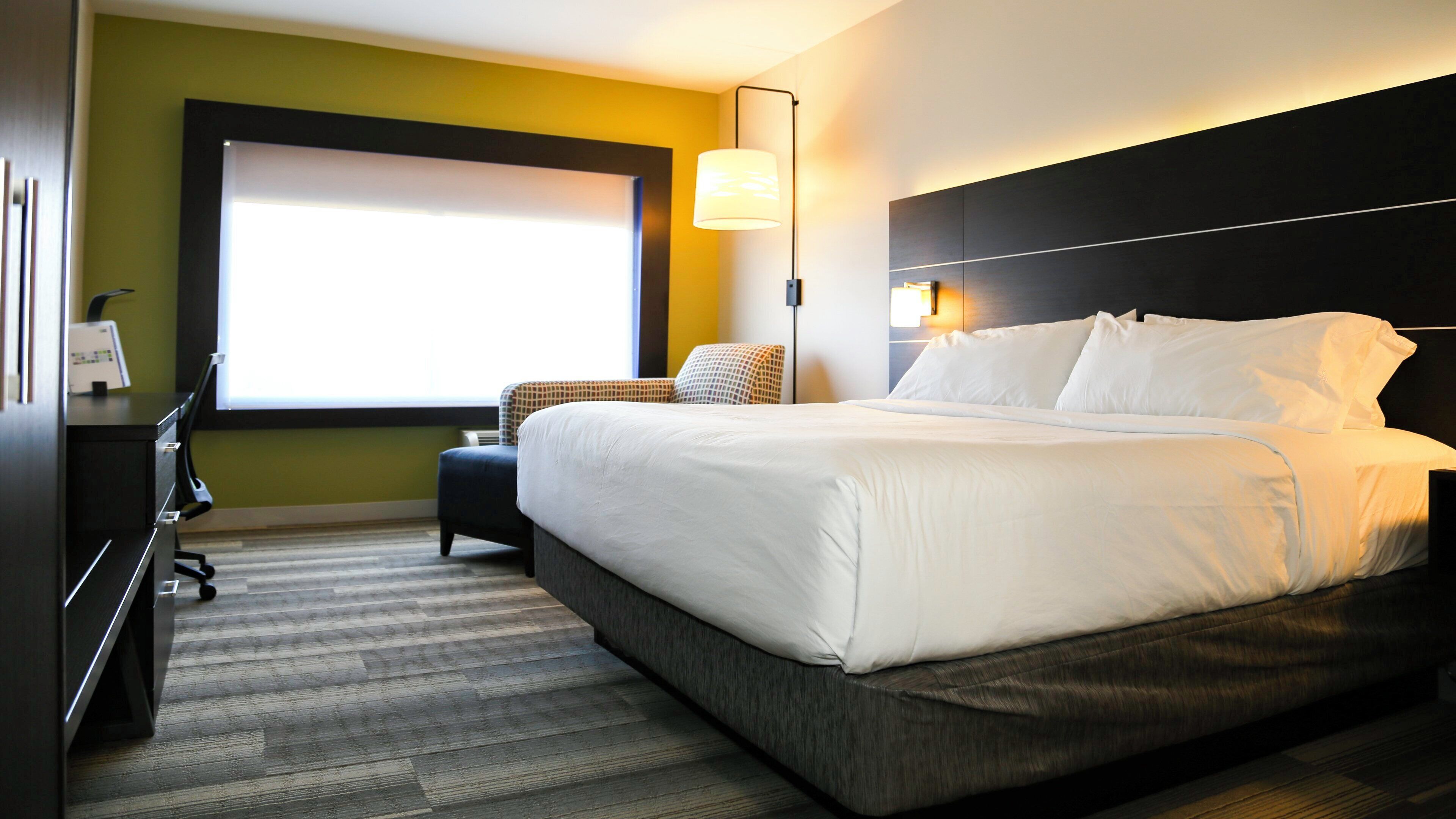 Habitación de hotel con una cama grande, un escritorio, una silla y un ventanal.