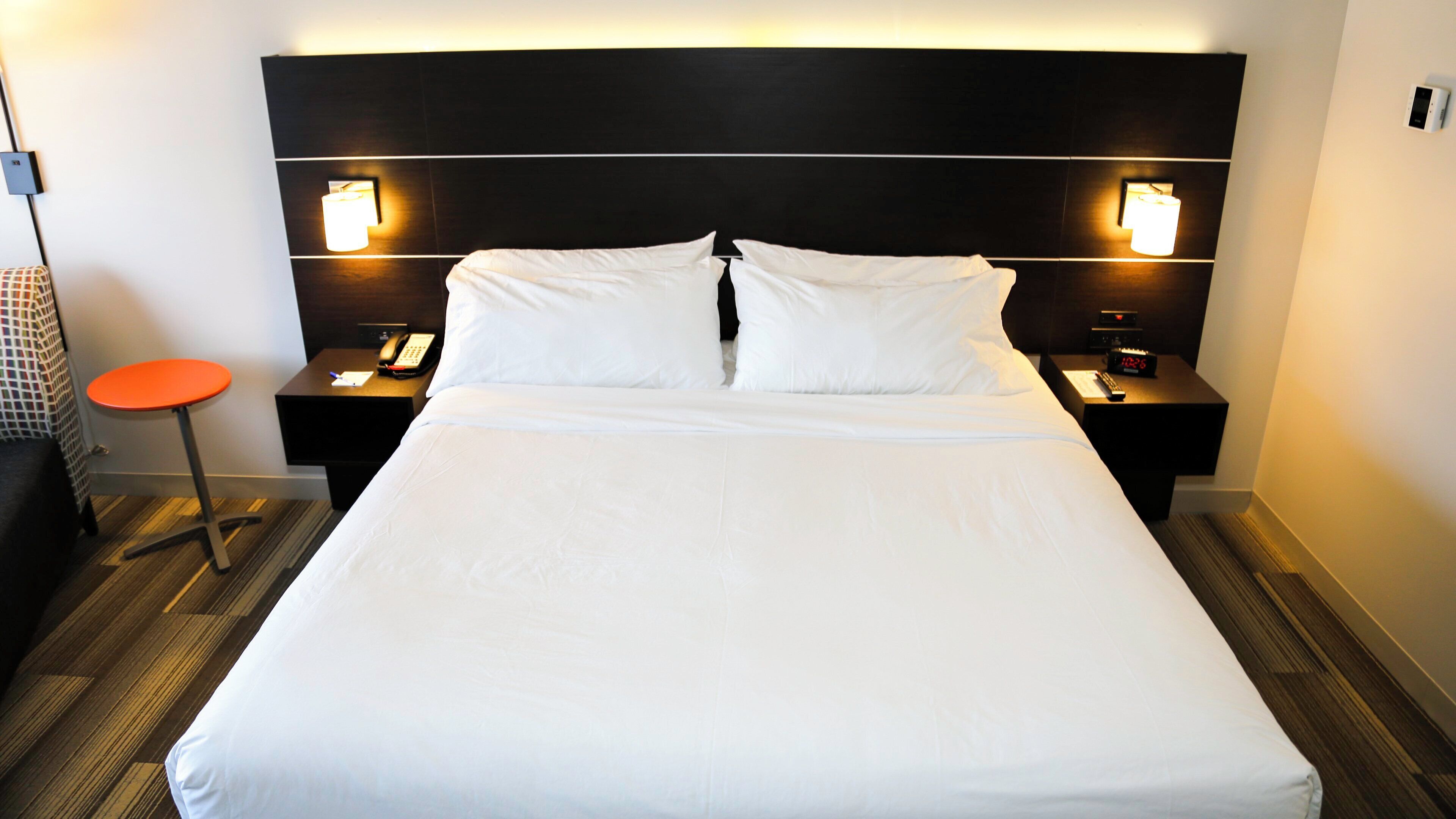 A hotel room with a large bed, two bedside tables, a nightstand, a telephone, and a small orange stool.