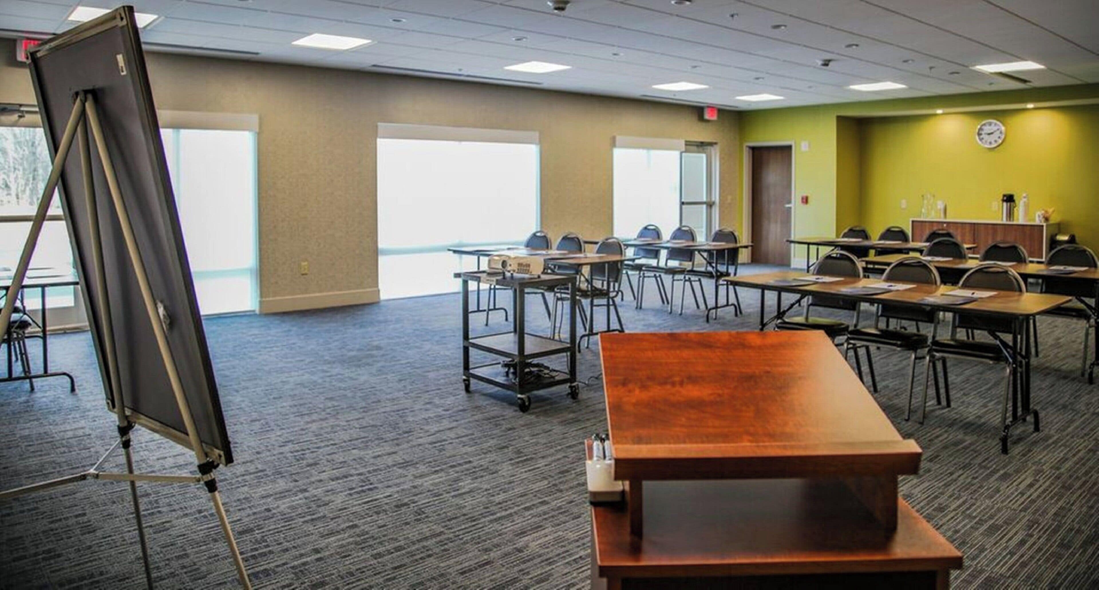 A conference room with a large projection screen, multiple tables, and chairs arranged for meetings.