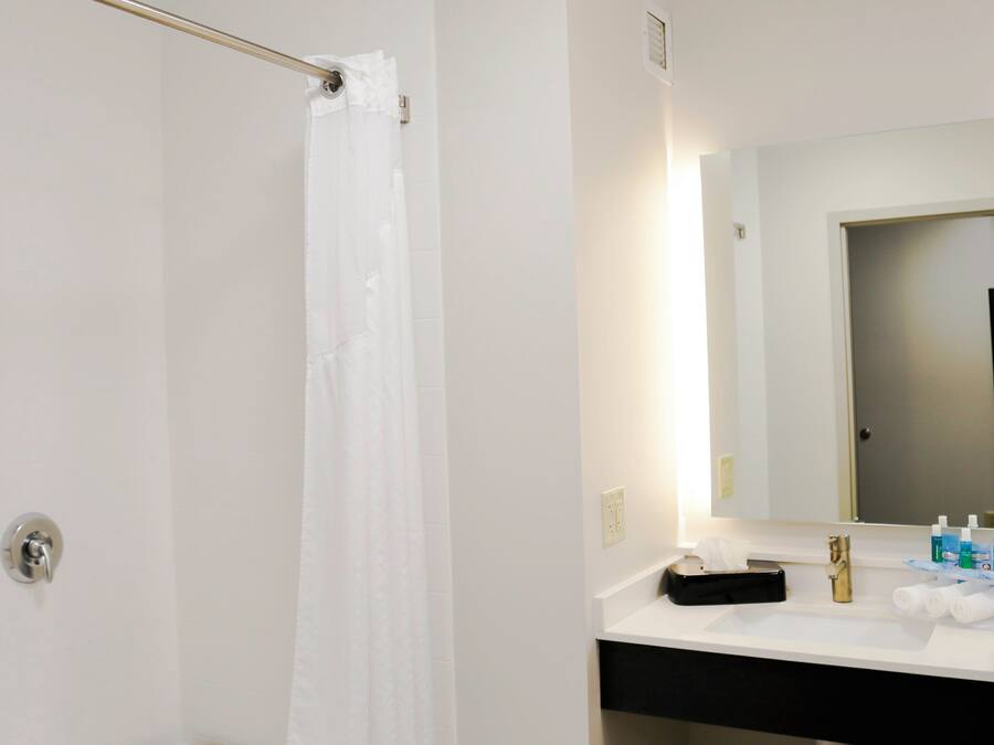 A bathroom with a shower, a sink, a mirror, and toiletries.