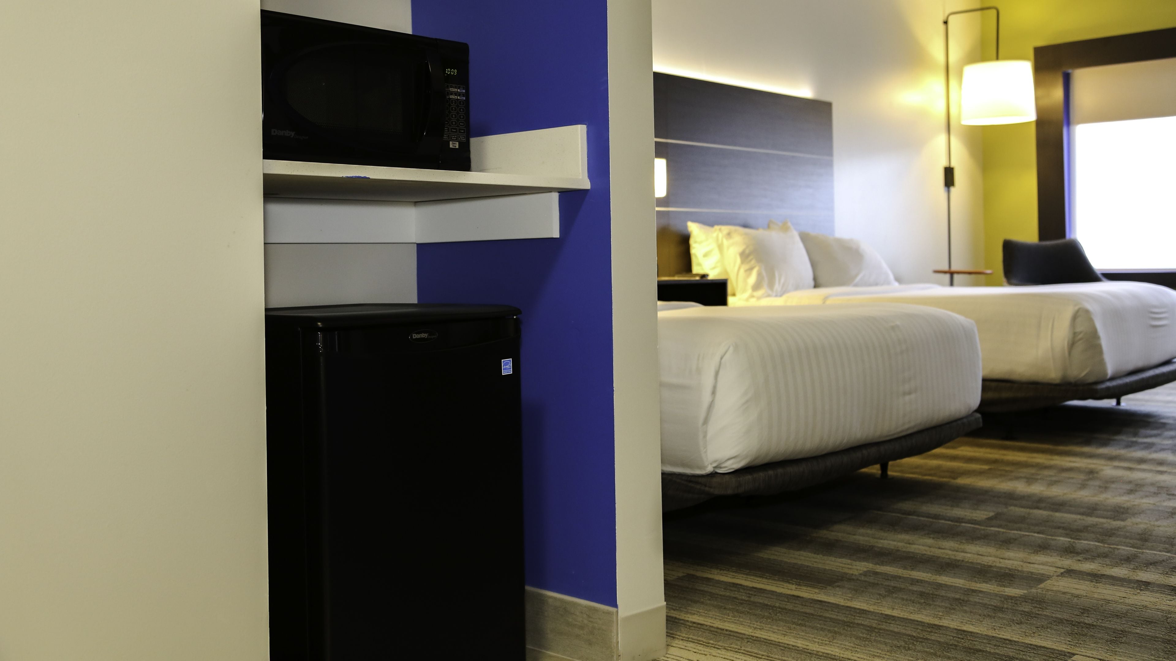 A hotel room with a bed, a microwave, a mini fridge, and a bedside lamp.