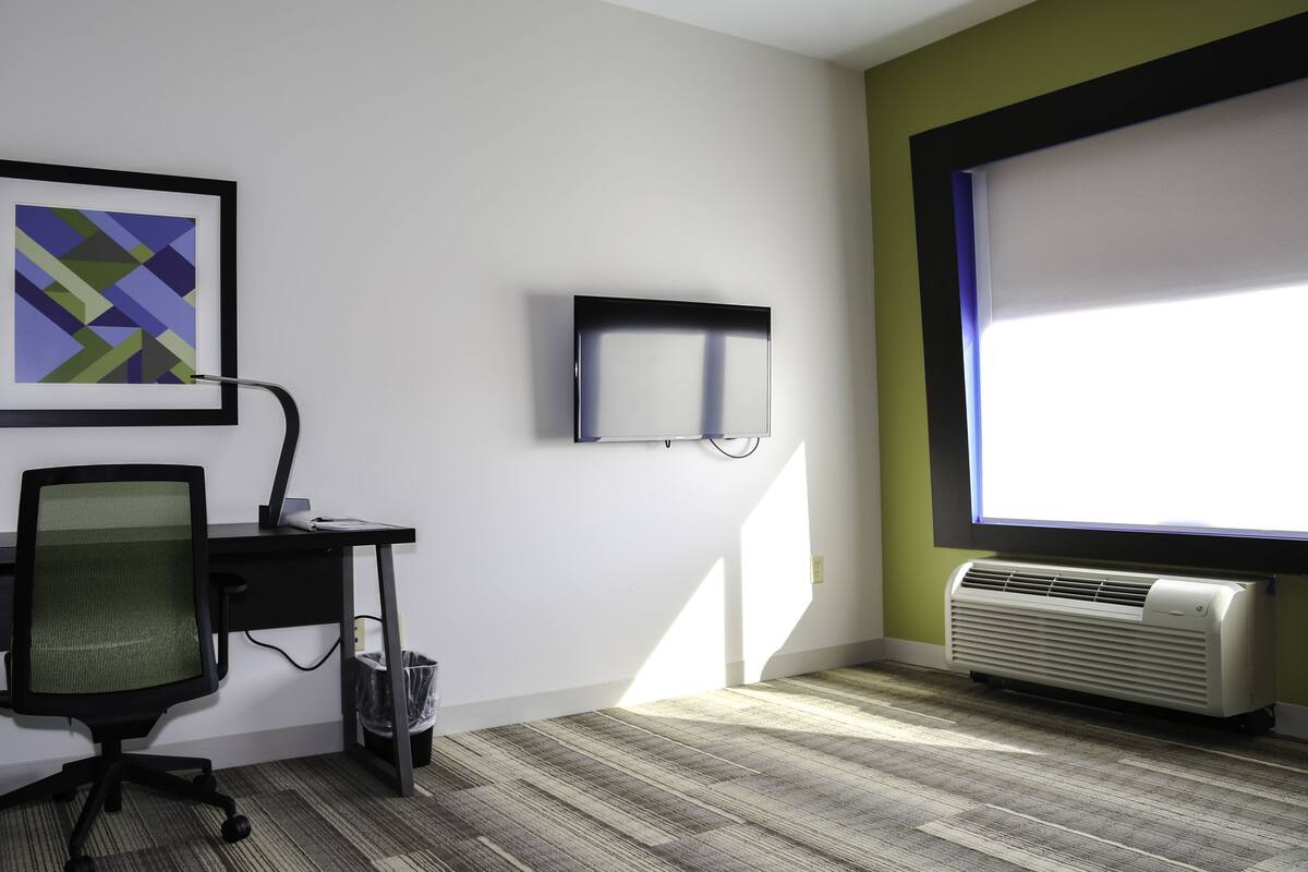 Un espacio de oficina moderno con escritorio, silla, obra de arte enmarcada, monitor de pantalla plana y ventana con persianas.