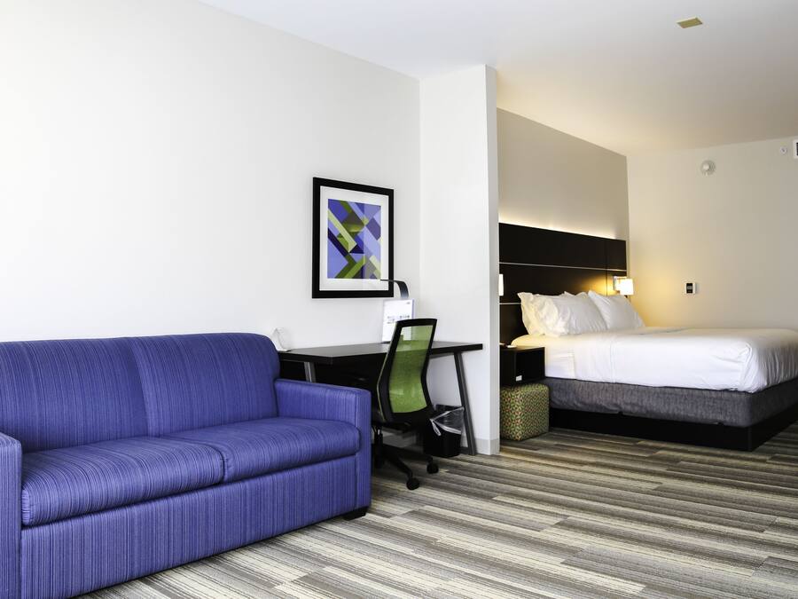 A hotel room with a blue sofa, a bed, a desk with a chair, and a framed picture on the wall.