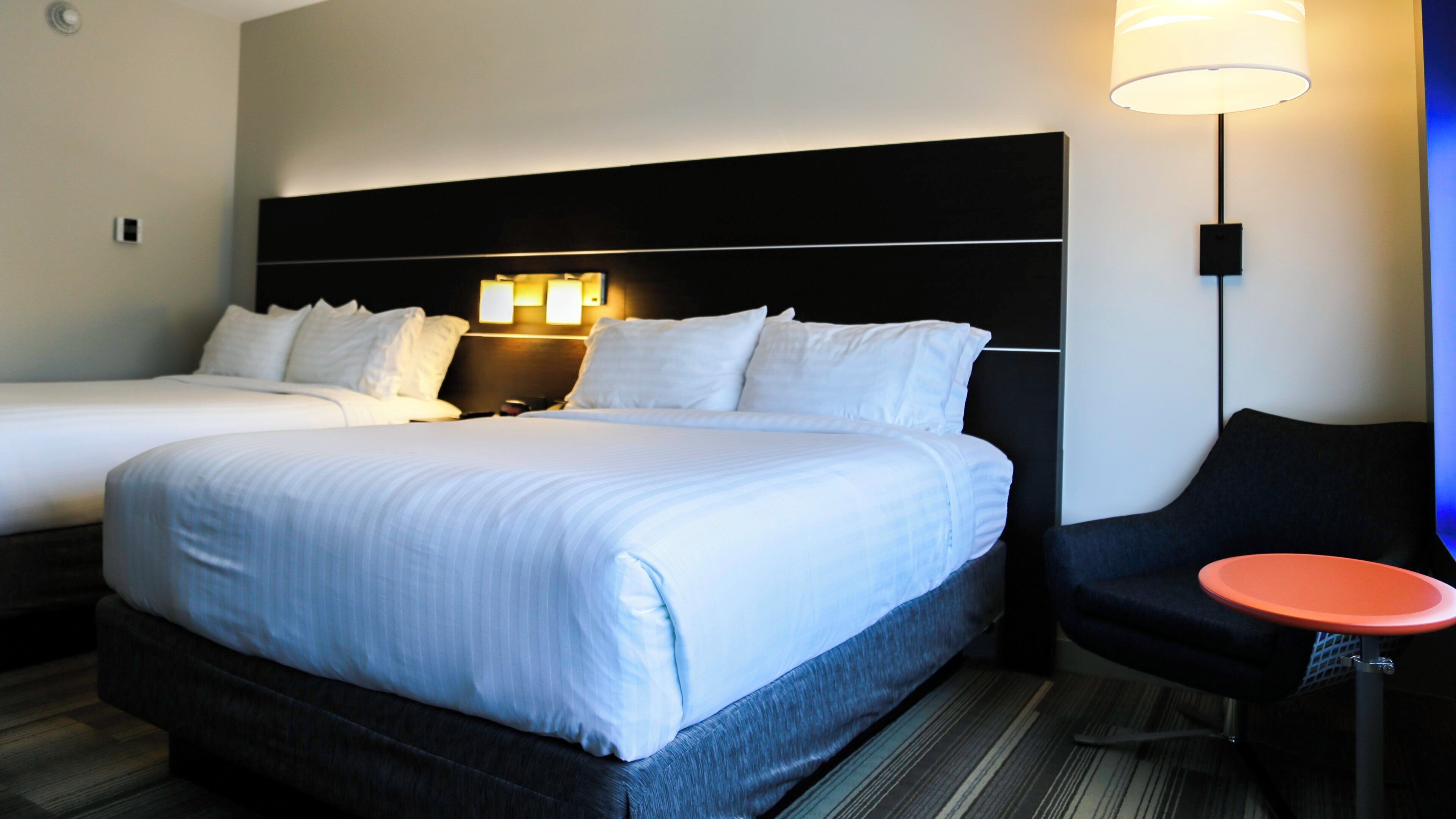 A hotel room with two beds, a nightstand, a lamp, and a small table.