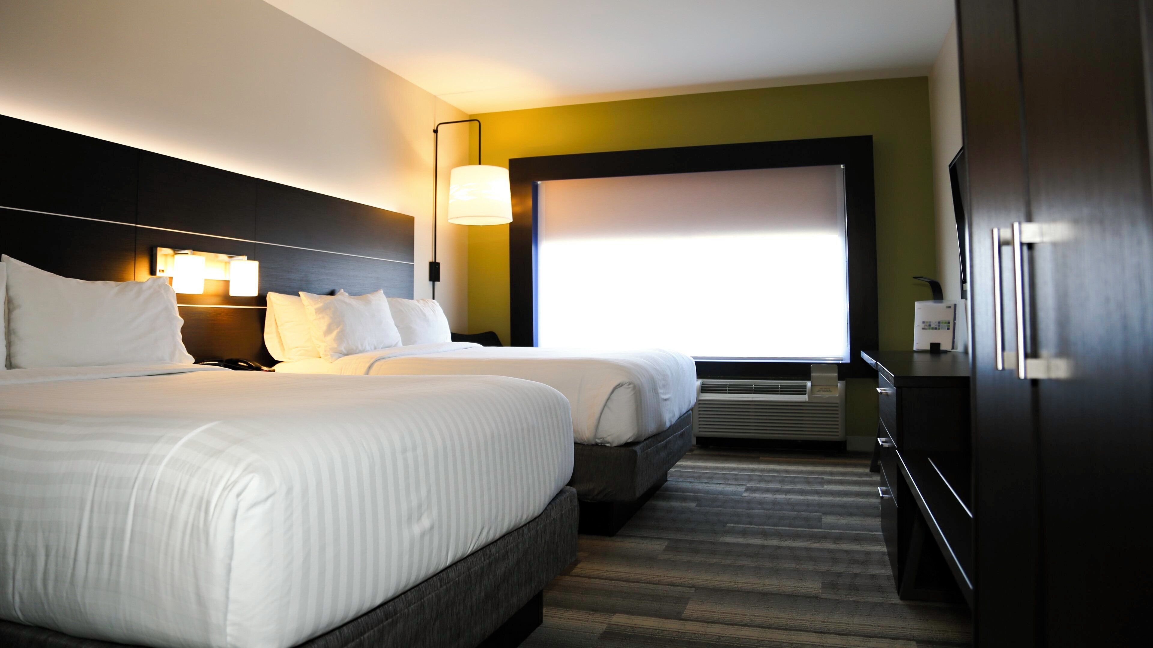 A hotel room with two beds, a large window, a flat-screen TV, and a minibar.