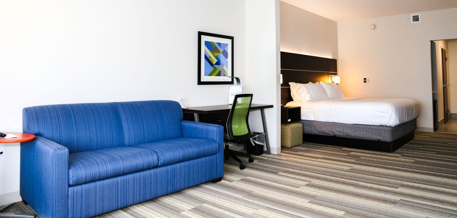 Una habitación de hotel con un sofá azul, un escritorio con computadora y una cama con ropa de cama blanca.