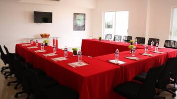 Un salón de conferencias con una larga mesa cubierta de rojo, rodeada de sillas negras, con botellas de agua y tarjetas de identificación sobre la mesa.