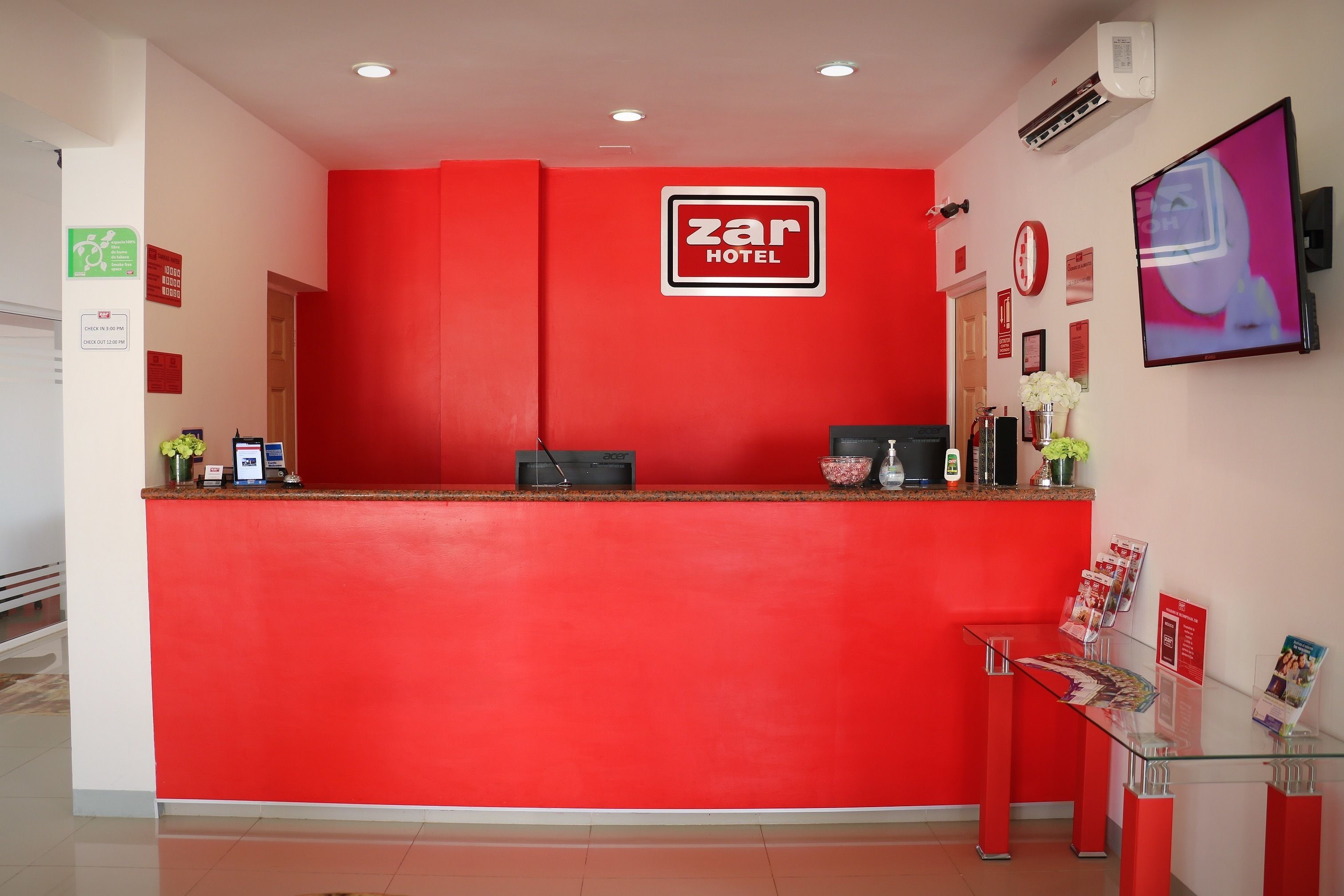 A hotel reception desk with a red color scheme, a digital screen, and a glass display case with brochures.