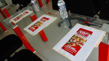 A glass table with a brochure for Zar Hotel, two water bottles, and red chairs.