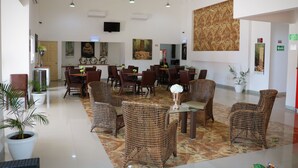 A spacious lobby with wicker furniture, a glass coffee table, and potted plants.