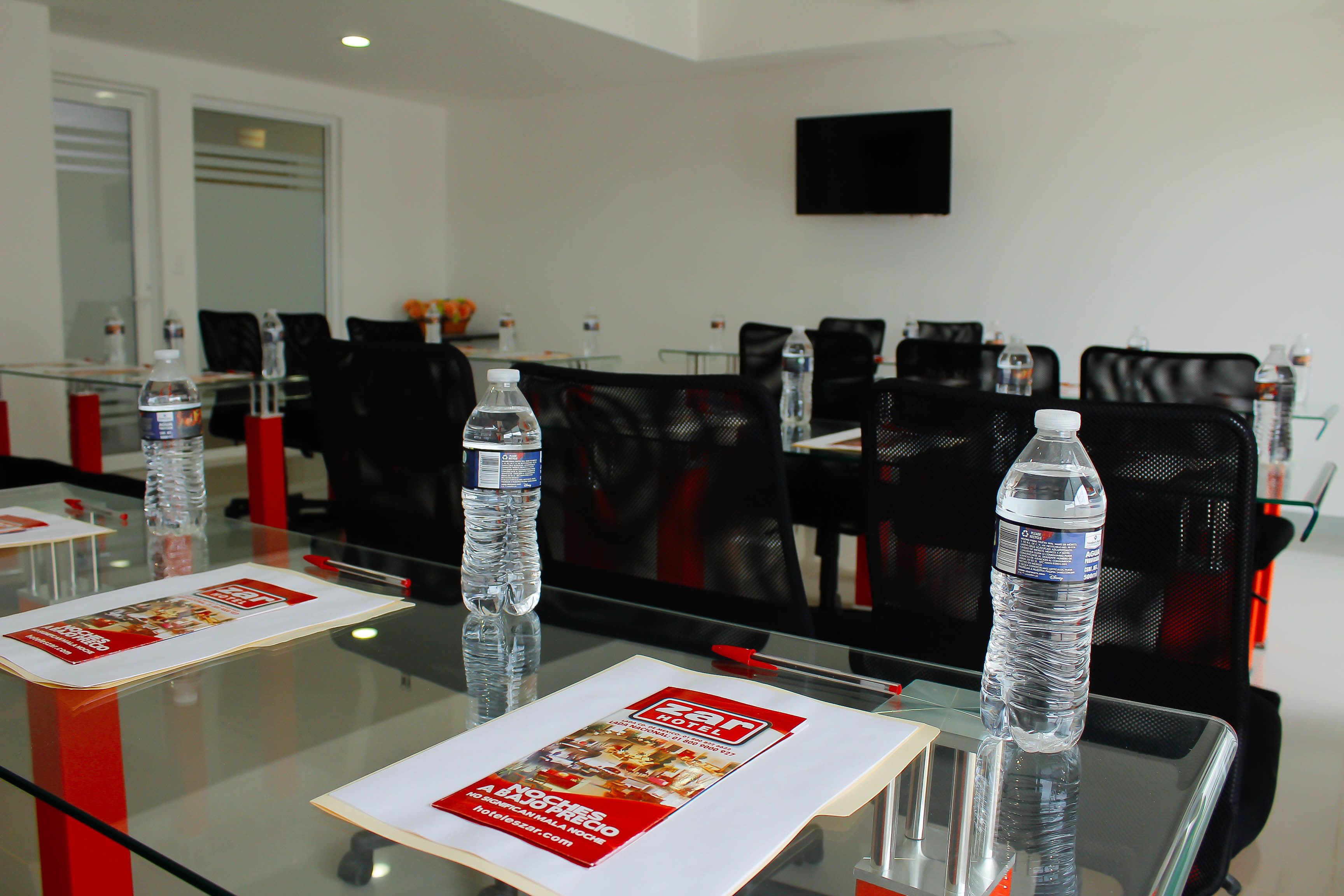 Un salón de conferencias con mesas de vidrio, botellas de agua y material promocional.