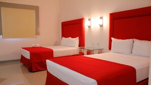 Two beds with red and white bedding, a small table, and a wall-mounted light fixture.