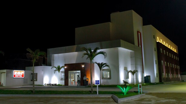 A modern hotel with a well-lit entrance, palm trees, and a sign indicating a handicap-accessible entrance.