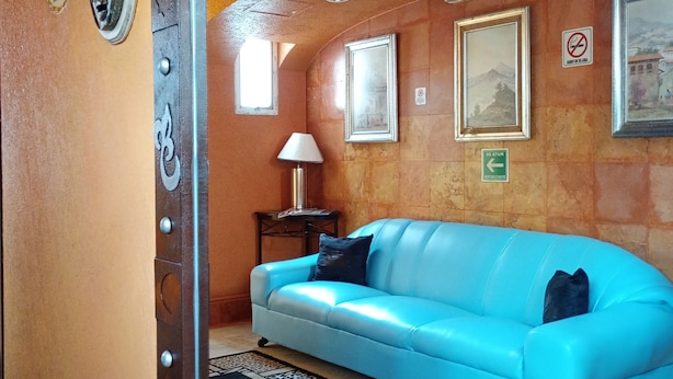 A room with a blue sofa, a lamp, framed pictures on the wall, and a mirror reflecting the room. - Hotel Real Azteca (Mexico City)