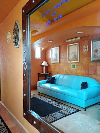 A room with a blue sofa, a lamp, framed pictures on the wall, and a mirror reflecting the room.