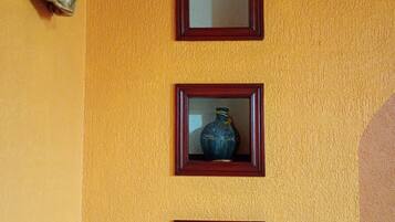A wall with three framed items: a vase, a skull-shaped vase, and a decorative angel.