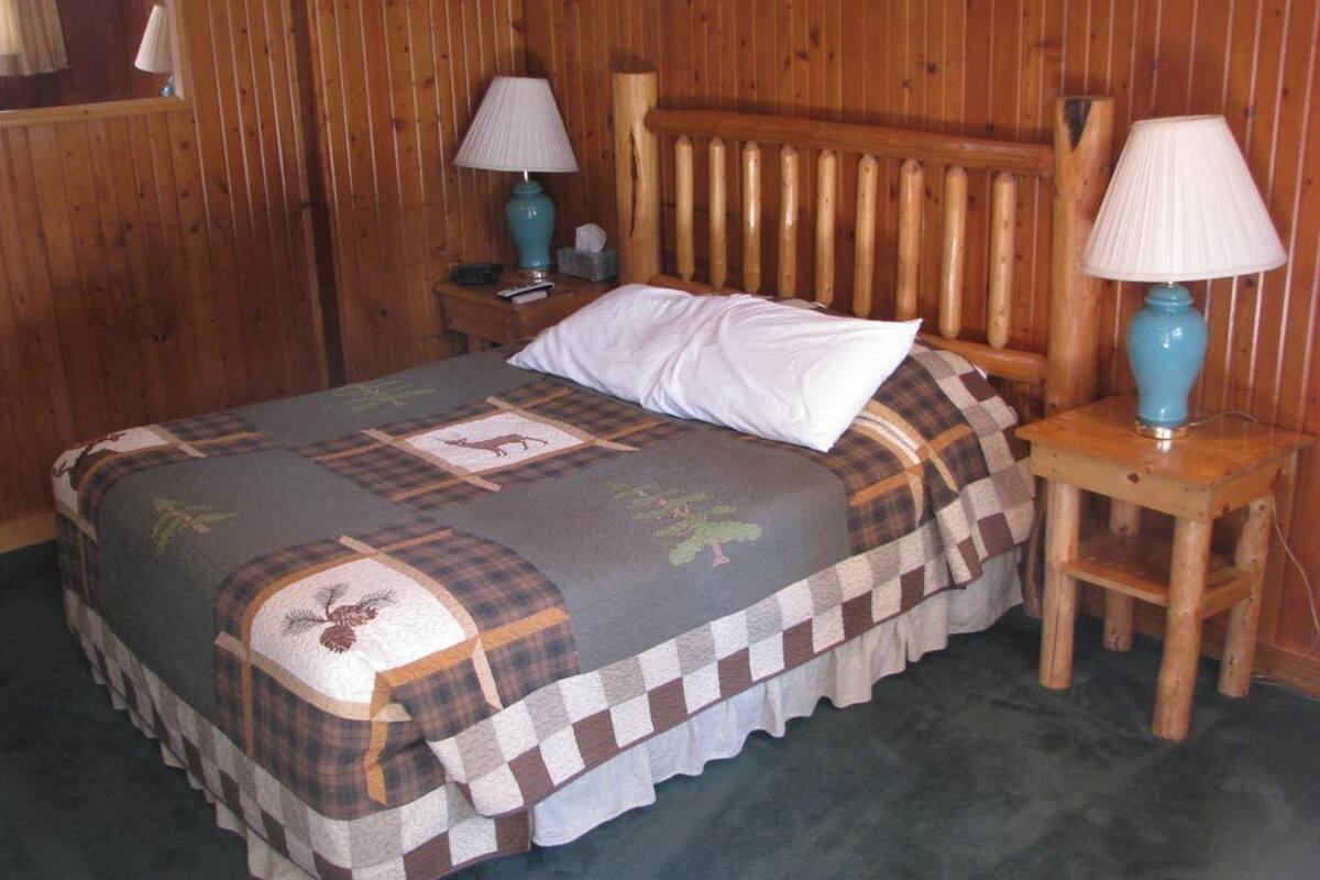 A wooden-paneled room with a bed, two nightstands, and two lamps.