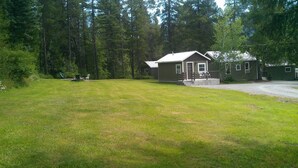 A building with a large grassy yard, a covered porch, and a gravel driveway. - Evergreen Motel (Coram)