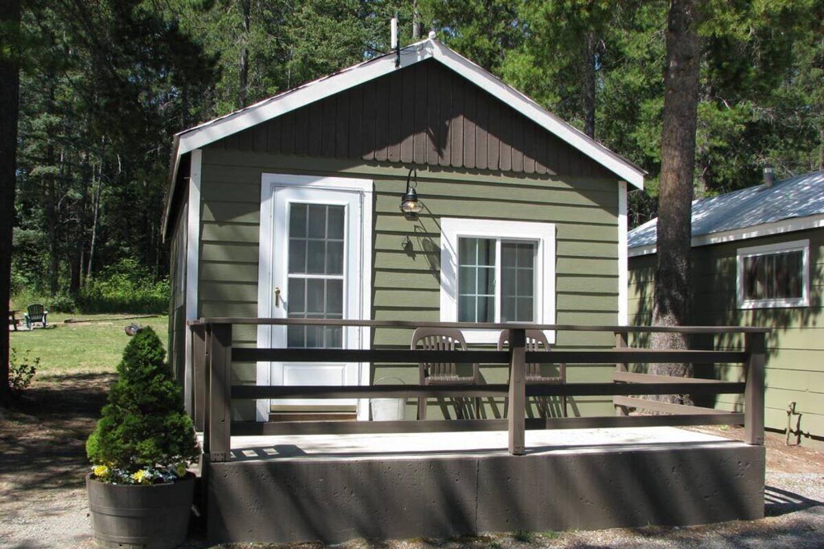 A small cabin with a porch, a small garden, and a view of the surrounding forest.