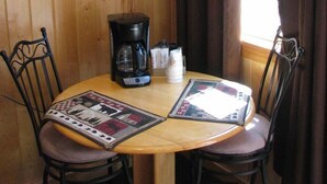 A wooden interior with a round table, two chairs, a coffee maker, a flat-screen TV, and a window with curtains. - Evergreen Motel (Coram)