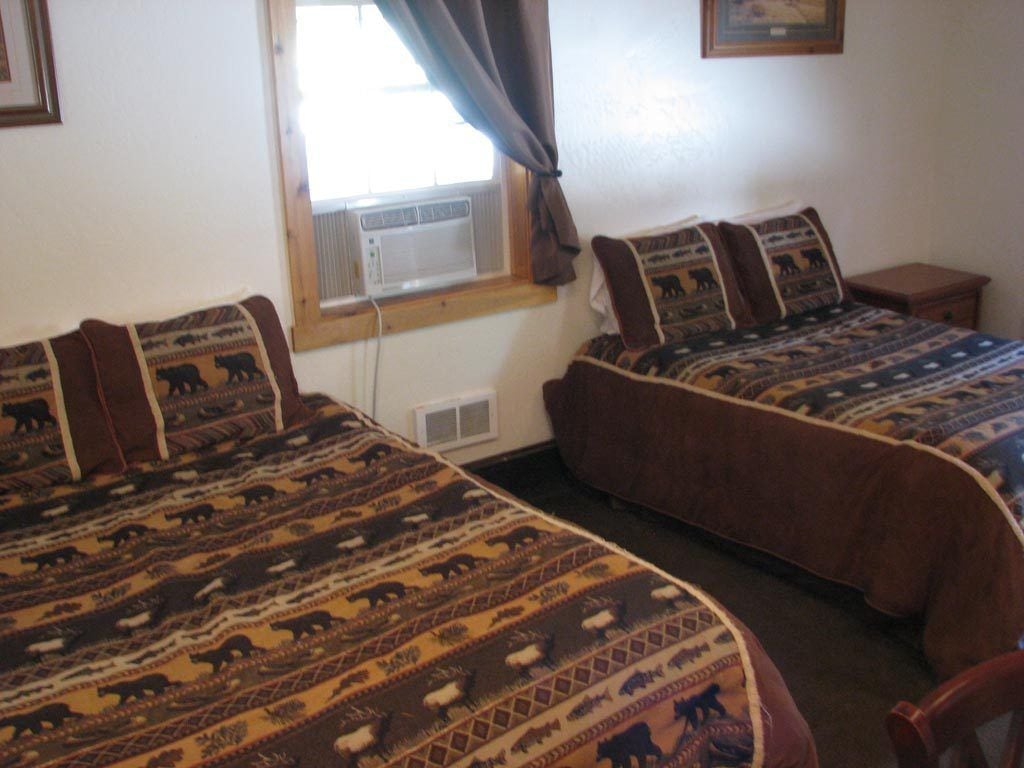 Une chambre avec deux lits, chacun agrémenté de draps et d’oreillers à motifs, une fenêtre avec des rideaux et une petite table de chevet.