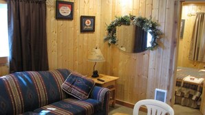 A cozy room with a wooden wall, a patterned sofa, a small table, and a white chair. - Evergreen Motel (Coram)