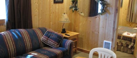 A cozy room with a wooden wall, a patterned sofa, a small table, and a white chair.