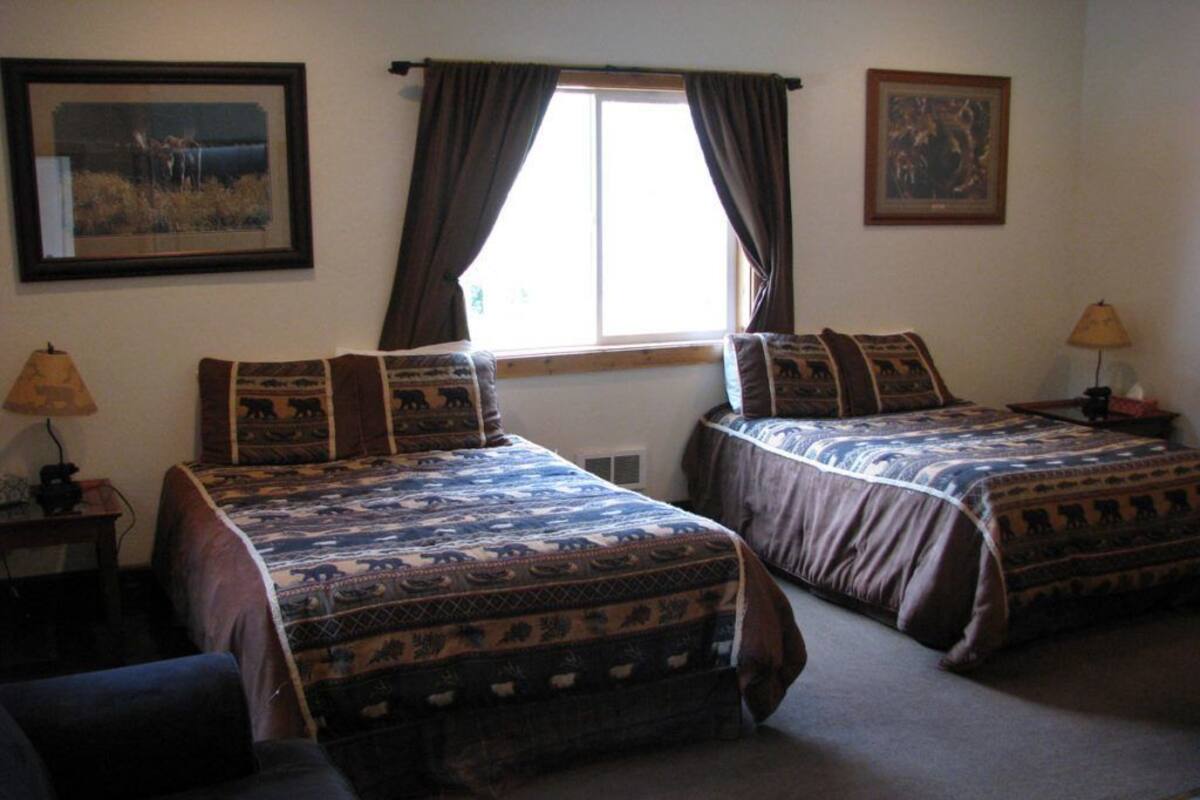 A room with two beds, a window with curtains, a lamp, and a framed picture on the wall.