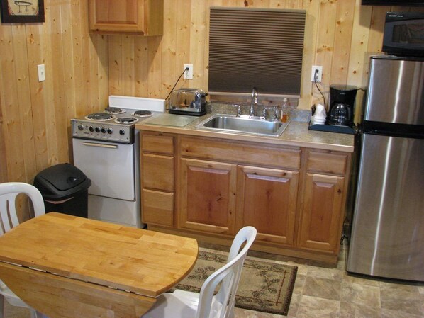 A compact kitchen with wooden cabinets, a stainless steel refrigerator, a stove, and a sink.