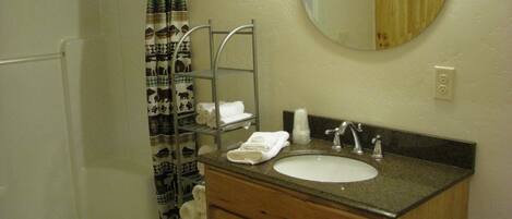 A bathroom with a shower, a sink, a mirror, and a towel rack.