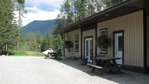 A building with a gravel driveway, a picnic table, and a mountain in the background. - Evergreen Motel (Coram)