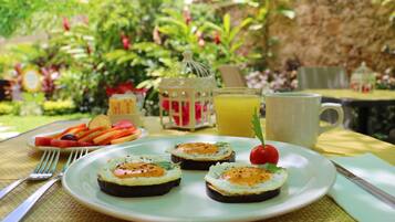 Un plato con tres huevos abiertos sobre tostadas, un tomate pequeño y una guarnición de fruta sobre una mesa al aire libre.