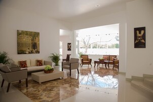 Un amplio salón con un sofá, sillones y una mesa de centro. En la pared hay un cuadro grande y una planta en maceta sobre la mesa.