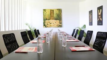 Un salón de conferencias con una larga mesa, sillas de malla negra, botellas de agua y folletos informativos.