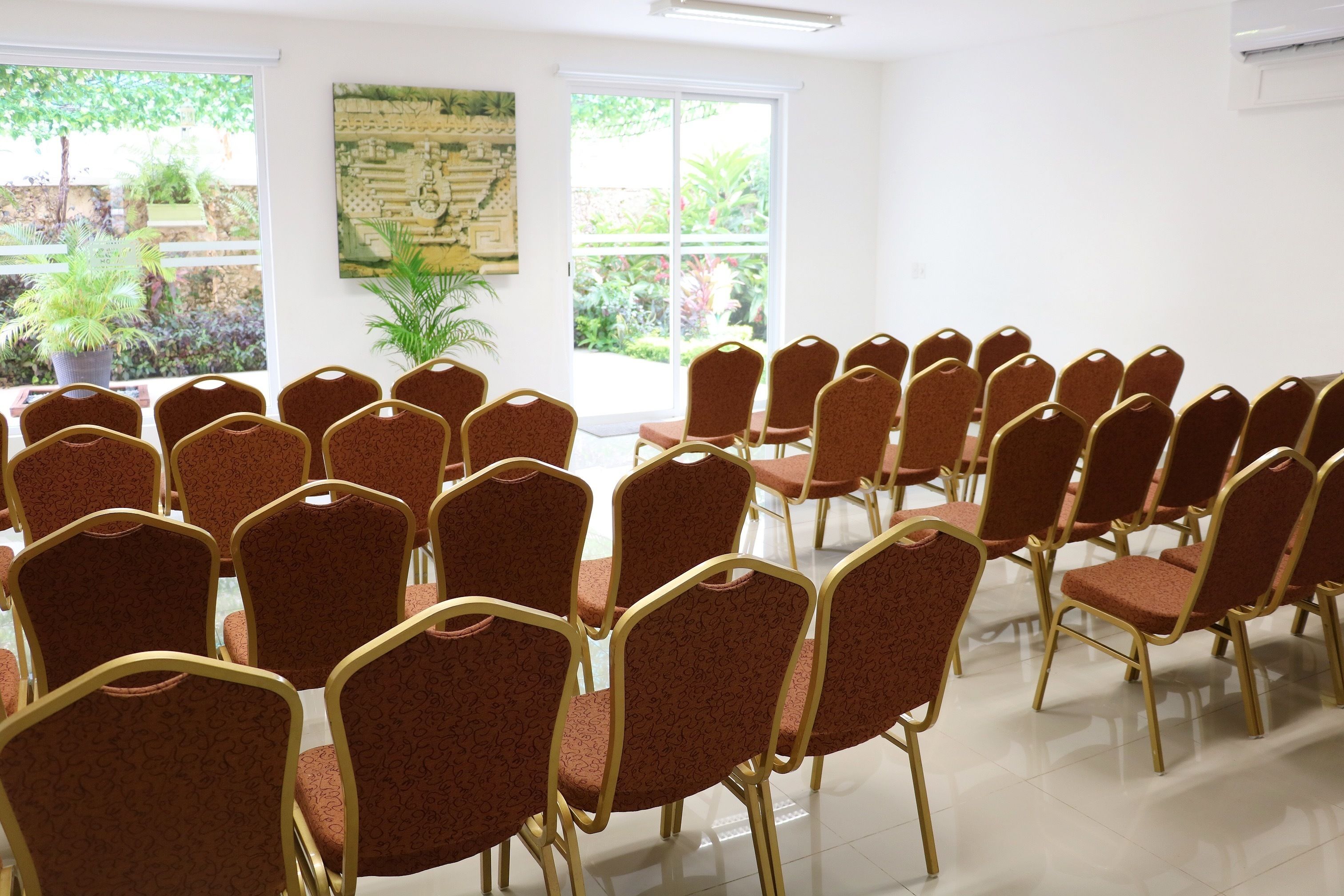 A conference room with rows of chairs, a large window with a view of greenery, and a wall-mounted map.