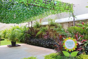 Un jardín exuberante con una variedad de plantas y un cartel que dice 'Ayudanos a cuidarlo Help us look after it'.