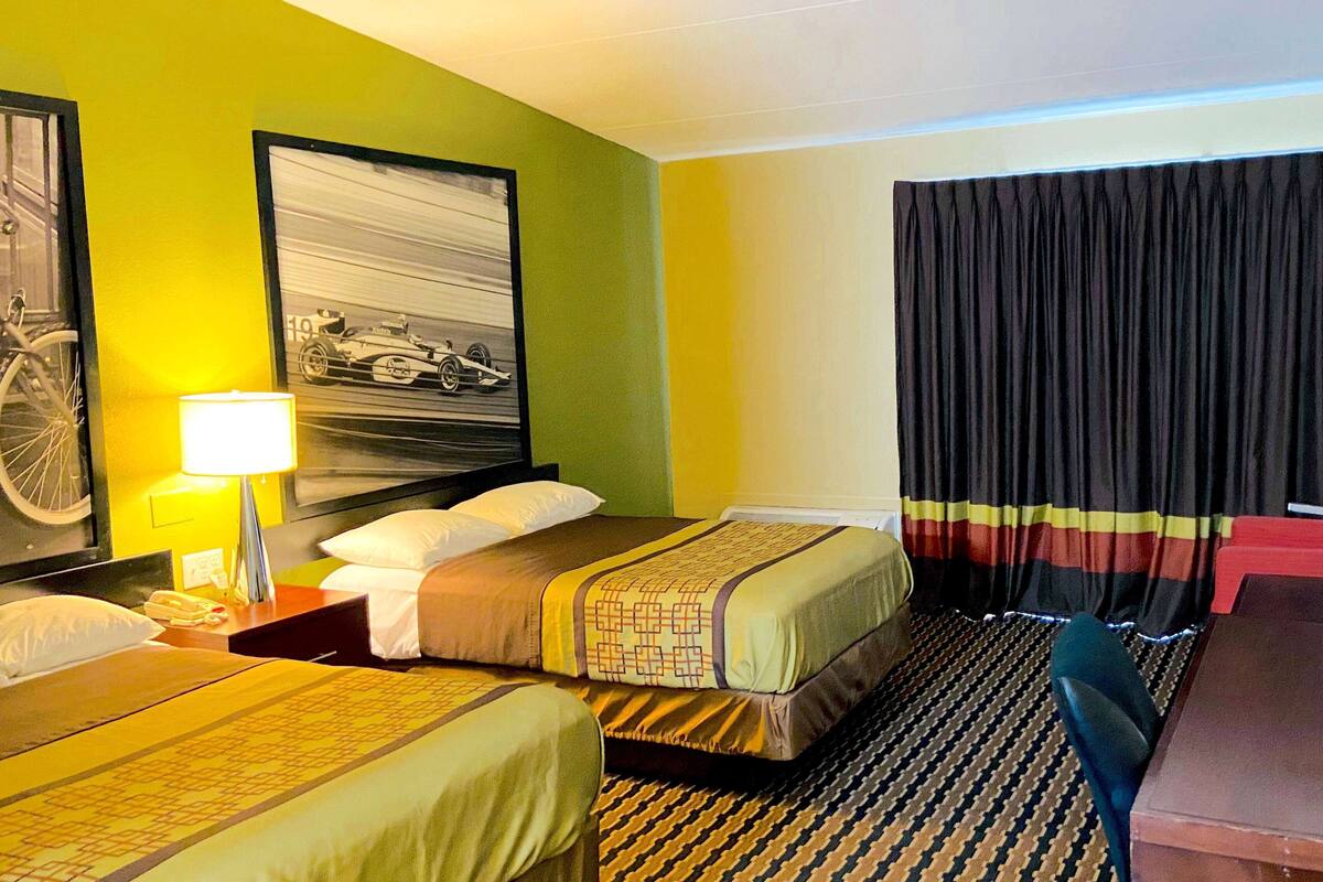 A hotel room with two beds, a large framed picture on the wall, a lamp, and a window with curtains.