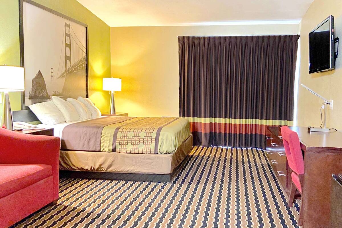 A hotel room with a bed, a desk, a chair, a TV, and a large window with curtains.