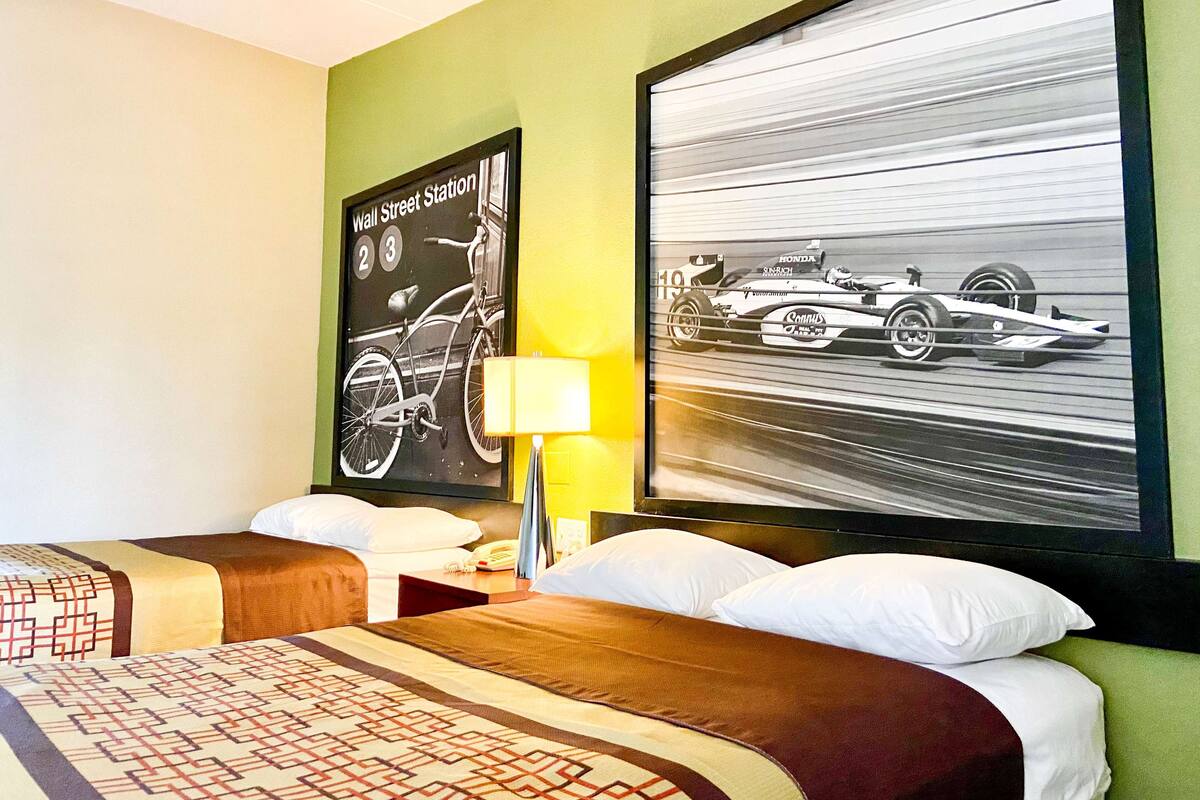 A hotel room with two beds, a wall clock, and a framed picture of a racing car.