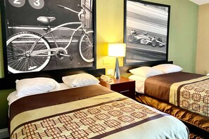 A hotel room with two beds, a nightstand with a lamp, and two large framed pictures on the wall.