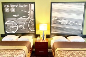 A hotel room with two beds, a nightstand with a lamp, and two framed pictures on the wall.