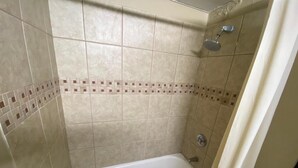 Um banheiro pequeno com azulejos, banheira e chuveiro.