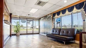 Um hall de hotel com piso de madeira, um sofá de couro preto e uma janela grande com vista para o exterior.