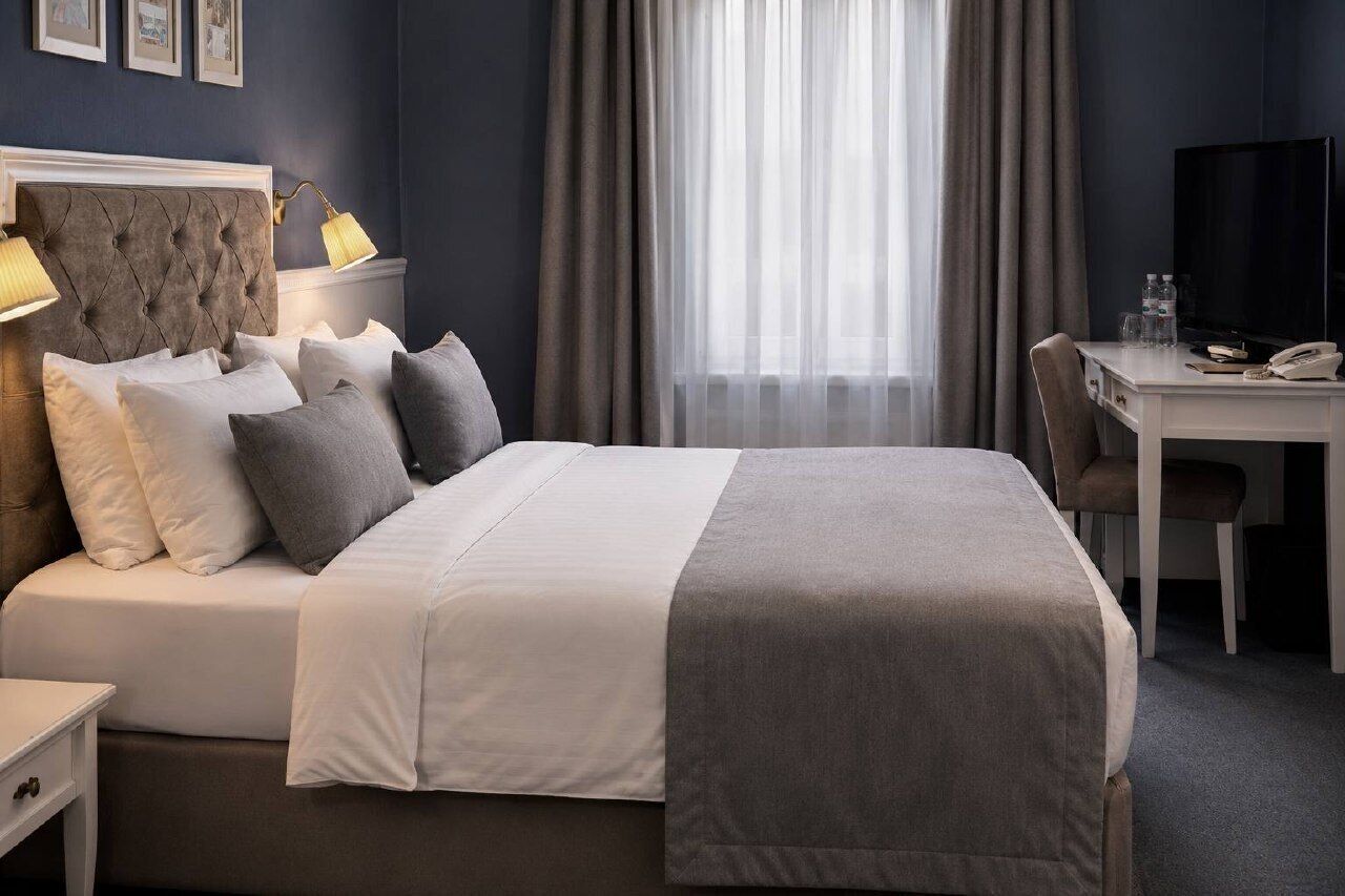 A hotel room with a bed, a desk, a chair, a television, and a window with curtains.