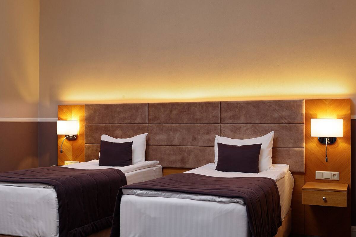 A hotel room with two beds, a wooden headboard, bedside lamps, and a wooden nightstand.
