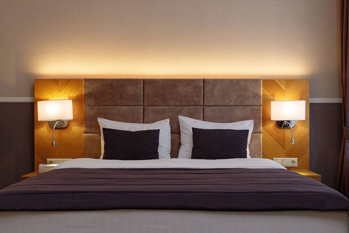 A hotel room with a large bed, two bedside lamps, and a wooden headboard.