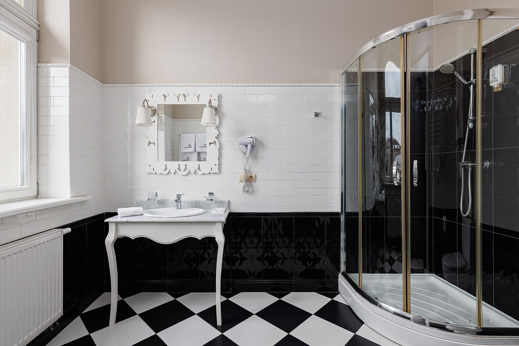 Un baño con tocador blanco, ducha con cerramiento de vidrio y piso a cuadros blanco y negro.
