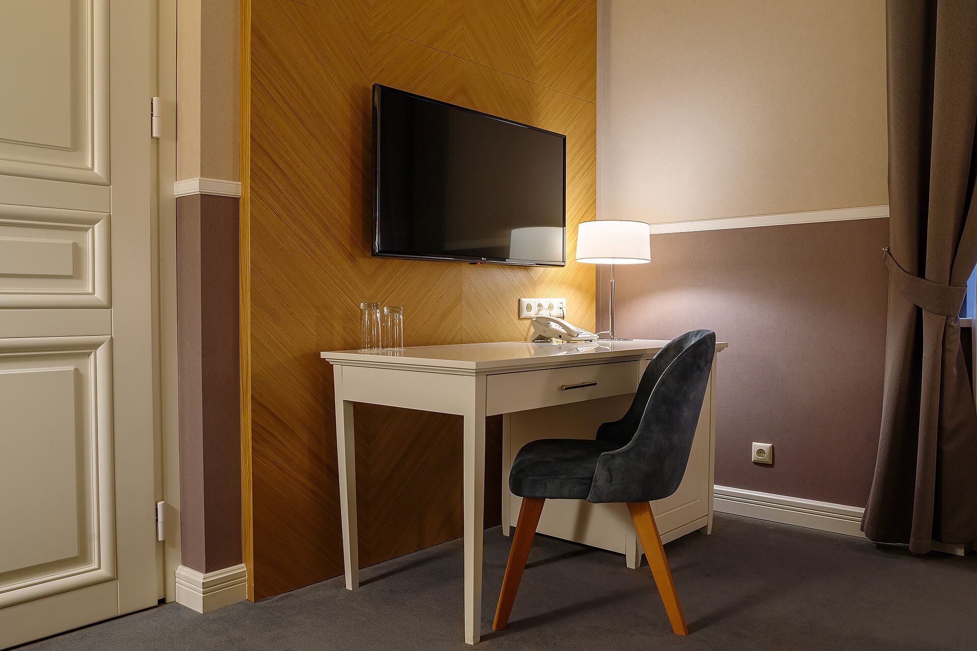 Ett hotellrum med ett skrivbord, en stol, en tv, en lampa och en telefon.
