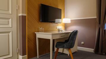 Ett hotellrum med ett skrivbord, en stol, en tv, en lampa och en telefon.
